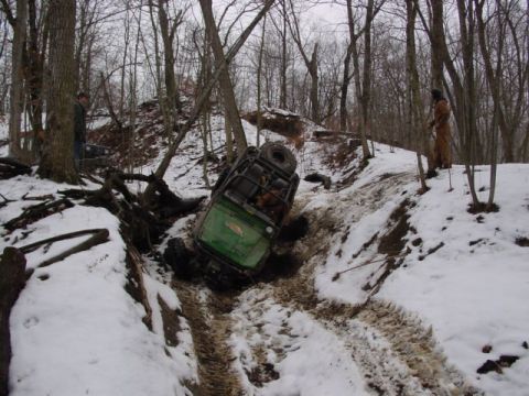 1992 Ford Bronco - A green off-road vehicle is stuck in a snowy ditch, with trees and snow-covered ground surrounding it.