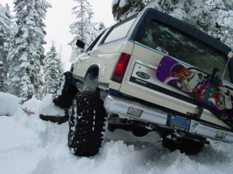 1986 Ford Bronco - 1986 Ford Bronco navigating a snowy mountain road with a snowboard mounted on the back.