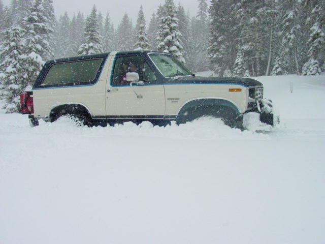 White and blue Ford Bronco stuck in deep snow, front right tire visible