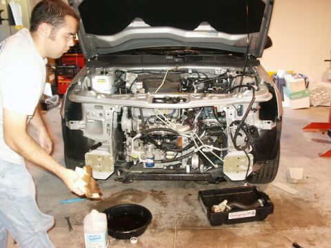 1994 Ford Bronco - A mechanic works on the exposed engine bay of a car, with tools and fluids nearby.