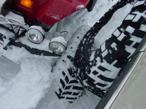 1986 Ford Bronco - A red SUV is partially buried in snow, with its large tires visible.