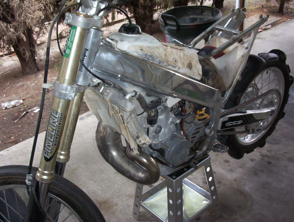 Dirt bike on stand, front forks labeled FINELINE SUSPENSION, engine exposed, chrome tank