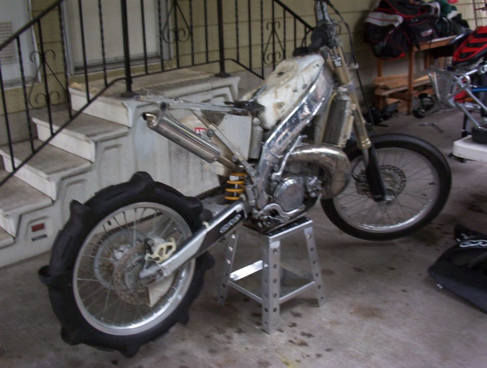 Dirt bike disassembled on a stand, showing engine and rear sand tire
