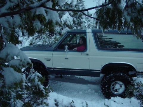 1986 Ford Bronco - A woman drives a white and blue 1987 Ford Bronco through a snowy, wooded area.
