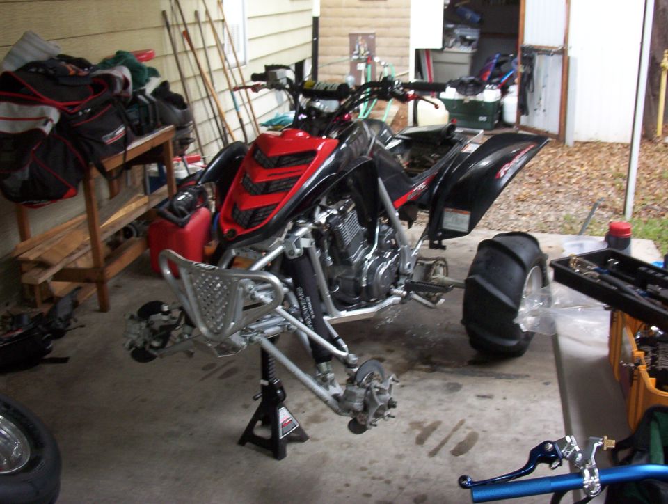 Black and red sport ATV on a jack stand with front wheels removed in a cluttered garage