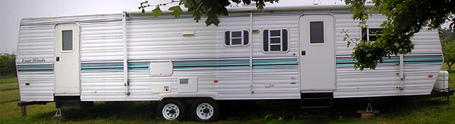 White Four Winds travel trailer with teal stripes parked on grass