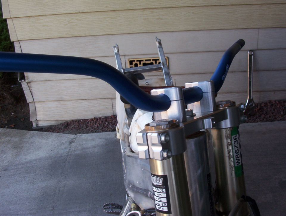 Close-up of blue handlebars and gold front forks on a motorcycle. Green sticker with W86Z36 visible