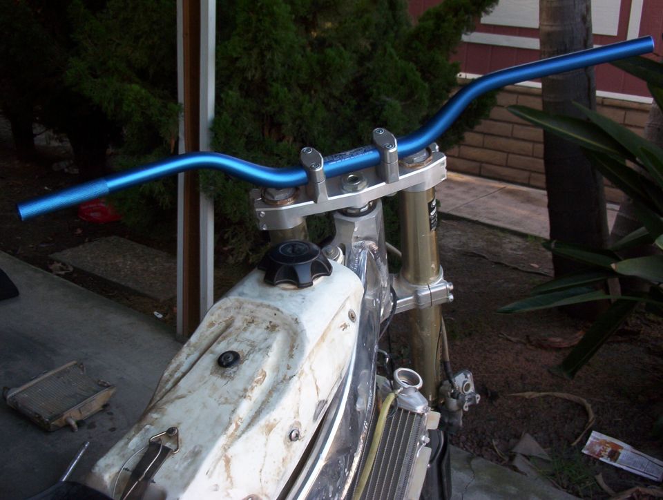 Blue handlebars and white fuel tank of a dirt bike, with a radiator visible