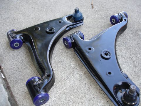 1989 Mazda MX-6 - Pair of aftermarket control arms with performance bushings, likely for suspension upgrade.
