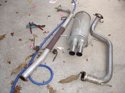 1989 Mazda MX-6 - Exhaust system components are disassembled and placed on the ground next to some tools and fallen leaves.