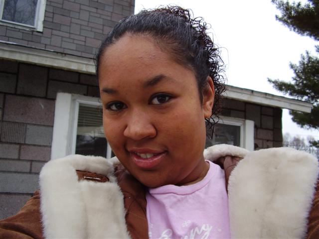 Woman in a pink shirt and brown jacket with white fur trim smiles for the camera