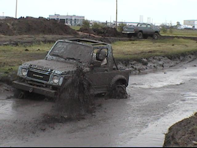 Mud-covered doorless Suzuki Samurai driving out of a flooded mud trench