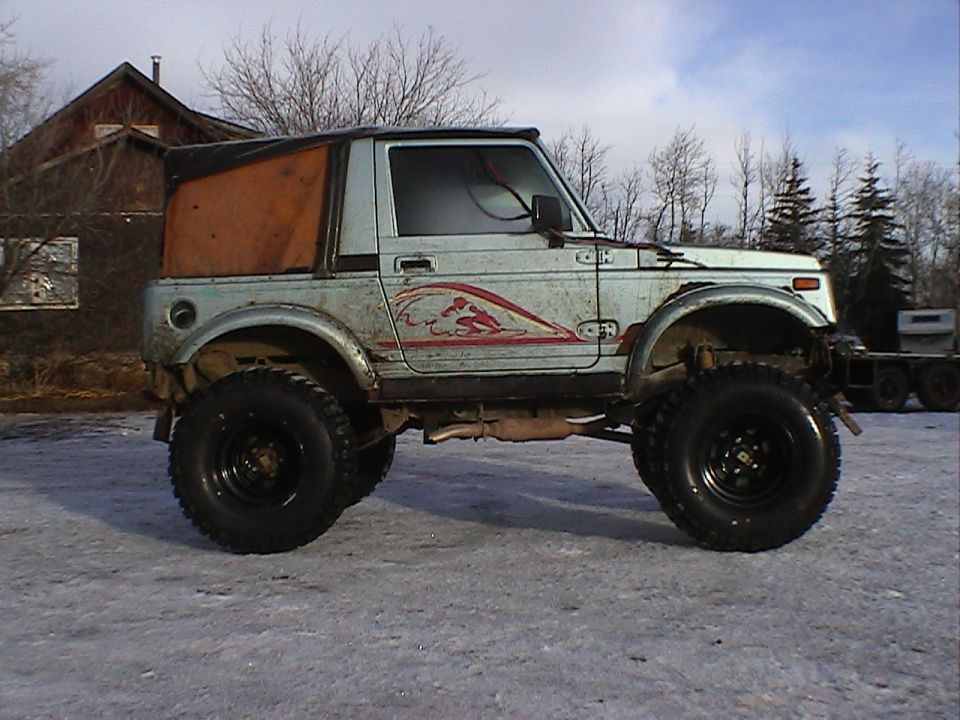 Lifted white compact SUV with soft top and large mud tires, side view, parked on snowy ground