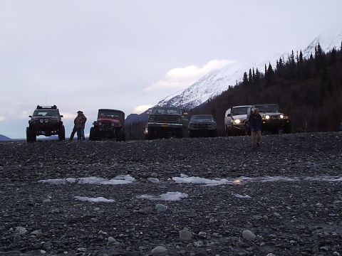 2000 Ford E350 - A group of off-road vehicles are gathered on a rocky terrain with a mountain range in the distance.