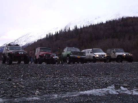 2000 Ford E350 - A group of off-road vehicles are parked on a rocky terrain with a mountain range in the distance.