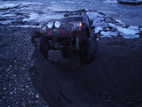 2000 Ford E350 - Off-road Jeep Wrangler navigates a challenging terrain near a body of water with ice chunks.