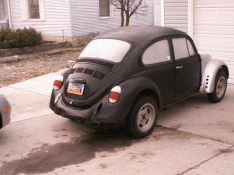 1975 Volkswagen Beetle - A black Volkswagen Beetle is parked in a driveway, showing its rear end and one silver fender.