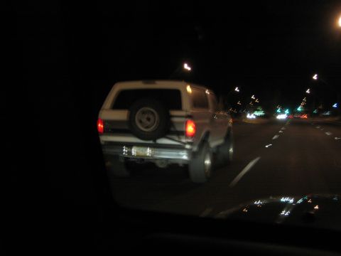 1968 Ford Mustang - Rear view of a white SUV with a spare tire on the back, driving on a highway at night.