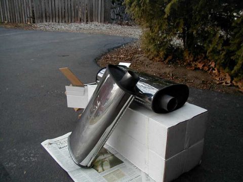 1997 Ford Taurus - A shiny chrome exhaust tip rests on stacked cardboard boxes, with a newspaper visible beneath.
