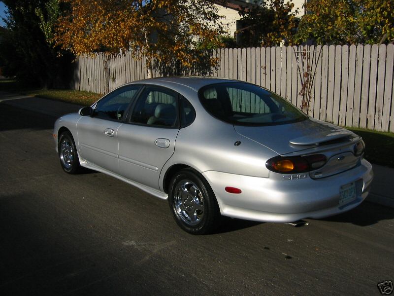 Silver Ford Taurus SHO sedan, rear three-quarter view, parked by wooden fence with fall foliage