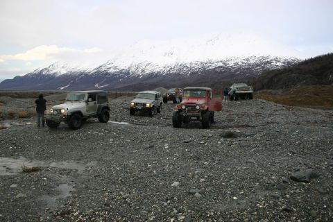 2003 Jeep TJ - Several off-road vehicles, including a red Toyota Land Cruiser and a white Jeep, navigate a rocky terrain with a snow-capped mountain in th…