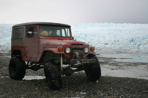 2003 Jeep TJ - A red Toyota Land Cruiser FJ40 sits on a rocky shore with a large glacier in the background.