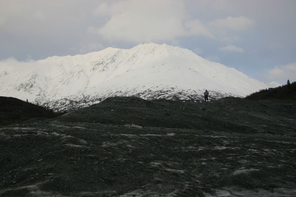 Person stands on a rocky hill with a snow-covered mountain range in the background