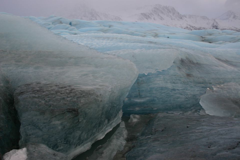 blue and gray ice formations with snow-covered mountains in background