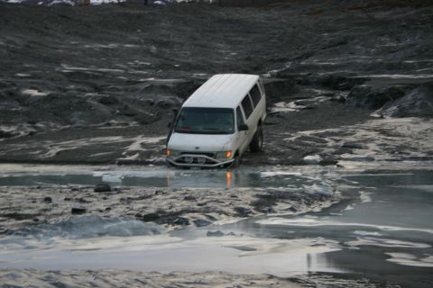 2003 Jeep TJ - A white van navigates through shallow, icy water on a desolate, rocky terrain.