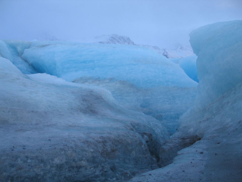 Close-up view of blue ice formations and crevasses on a glacier with misty mountains in the background
