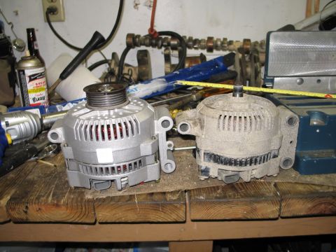 1995 Ford Bronco - Comparison of a new alternator next to a used one on a workbench.