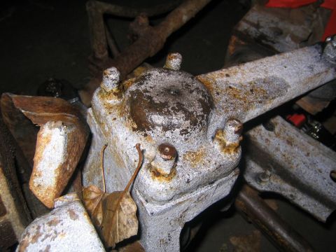 1978 Ford Bronco - This image shows a close-up of a heavily rusted and painted vehicle suspension component, with dried leaves nearby.