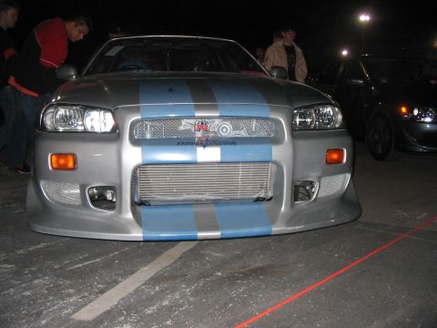 1986 Ford Bronco - A silver Nissan Skyline GT-R with blue racing stripes is parked on asphalt at night.