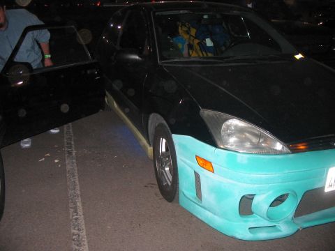 1986 Ford Bronco - A black car with a distinctive teal front bumper and side skirts is parked next to another vehicle.