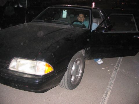 1986 Ford Bronco - This black 1987 Ford Mustang coupe has its driver's door open with a man seated inside.