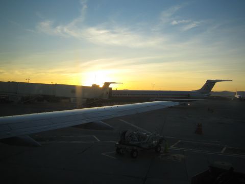 1968 Ford Mustang - The sun sets over an airport tarmac, casting long shadows on the ground near parked airplanes.