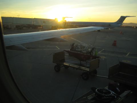 1968 Ford Mustang - An airplane is parked at an airport gate during a sunset, with luggage carts on the tarmac.
