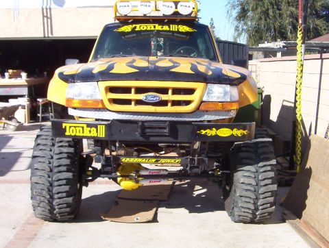 2000 Ford F-450 - Head-on view of a lifted yellow Ford pickup with black flame graphics, "Tonka III" lettering on the windshield banner and front bumper, and…
