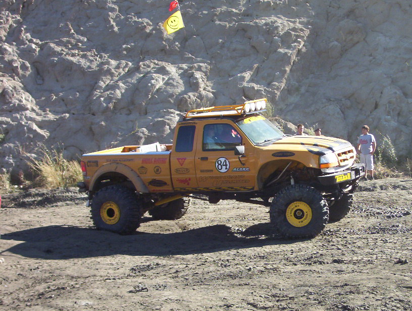 Yellow number 84 off-road pickup in profile on gravel by a rock face