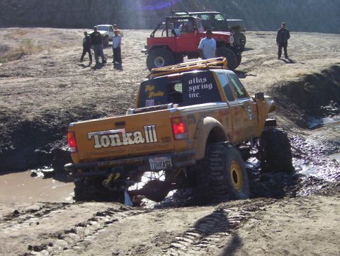 2000 Ford F-450 - Rear three-quarter view of a yellow off-road pickup working through a muddy rut, tailgate lettered 'Tonka III' and 'Woodworks Unlimited' wi…