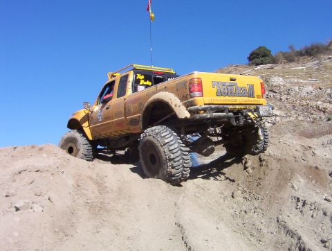 2000 Ford F-450 - Dust-covered yellow lifted extended-cab pickup with "Tonka II" tailgate lettering flexes over a dirt mound, showing its long-travel suspens…