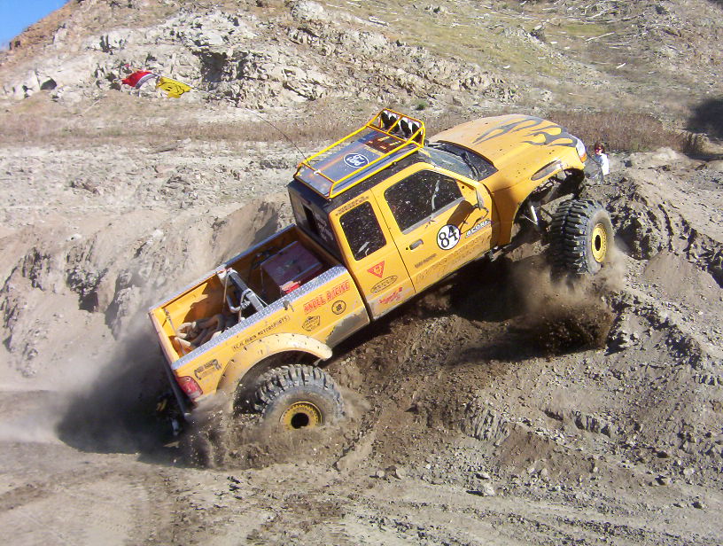 Yellow number 84 off-road pickup dropping down a steep dirt bank, tires spraying dirt