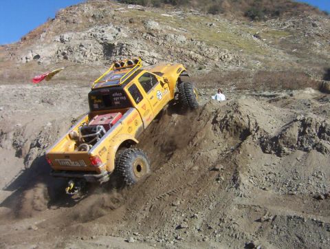 2000 Ford F-450 - Rear three-quarter view of a yellow lifted extended-cab pickup with "Tonka III" tailgate lettering perched nose-up on a steep rutted dirt b…