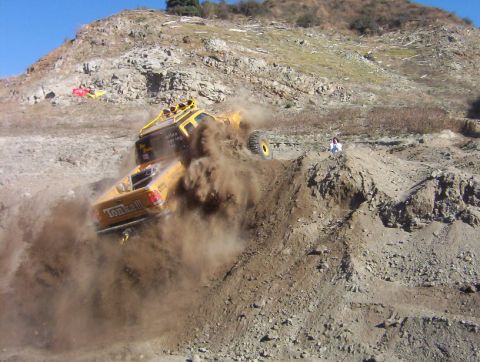 2000 Ford F-450 - A yellow tube-chassis rock buggy with a "Tonka" tailgate graphic climbs a steep dirt hill, front wheels lifted off the ground and a huge du…