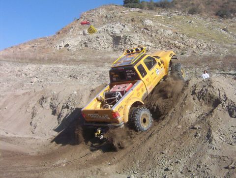 2000 Ford F-450 - A yellow lifted extended-cab pickup with "Tonka III" tailgate lettering and "Atlas Spring Inc" rear-window decal backs down a steep dirt ba…