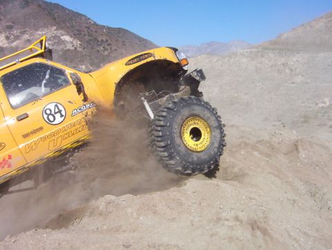 2000 Ford F-450 - A yellow 2000 Ford F-450 navigates a dusty, off-road terrain with its large tires.