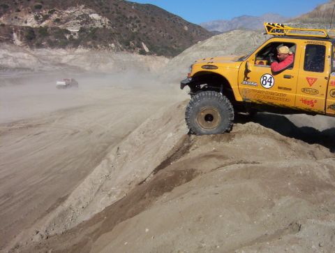 2000 Ford F-450 - Off-road vehicles navigating a dusty, hilly terrain under a clear sky.