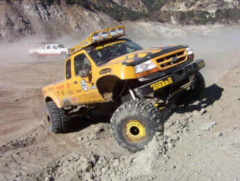 2000 Ford F-450 - Dusty yellow lifted Ford extended-cab pickup with black hood flames, race number 84 door roundel and "Tonka III" front bumper crawls over a…