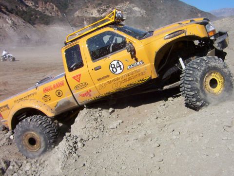 2000 Ford F-450 - Close side view of a yellow lifted extended-cab pickup climbing a rock ledge, front wheels up on the ledge with heavily lugged tires on gol…