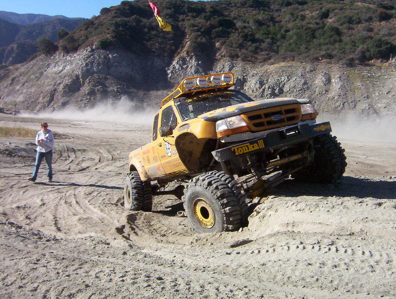 Yellow Ford Ranger off-road truck flexing on a dirt mound in a canyon